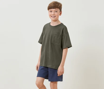 Junge trägt ein Kinder-Heavy-T-Shirt mit überschnittenen Schultern und blaue Shorts.