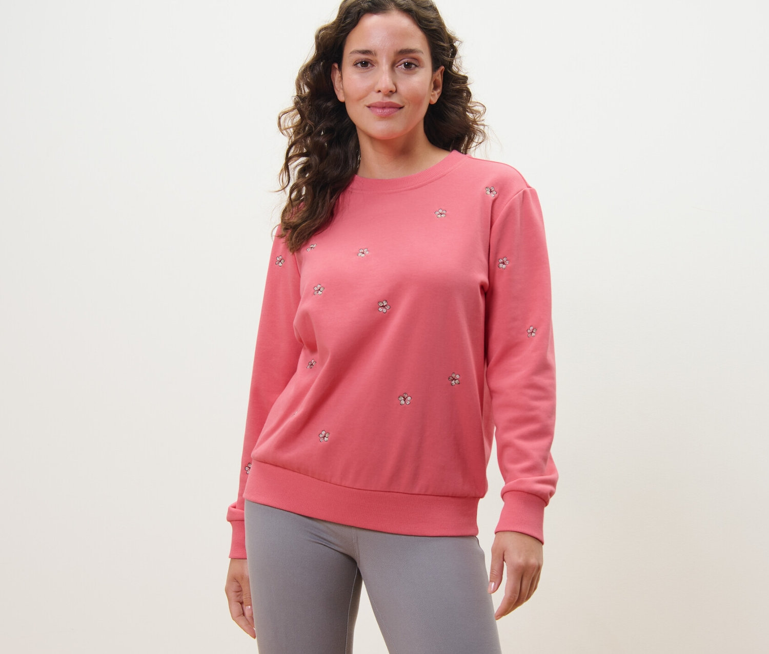 Frau trägt ein besticktes Sweatshirt in Rosa und graue Leggings.