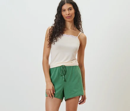 Frau posiert in hellem Top und grünen Shorts.