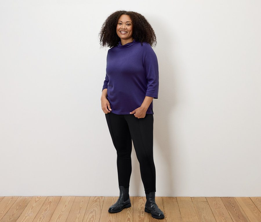 Frau posiert in schwarzen Heavy-Leggings mit Biese und lila Oberteil.