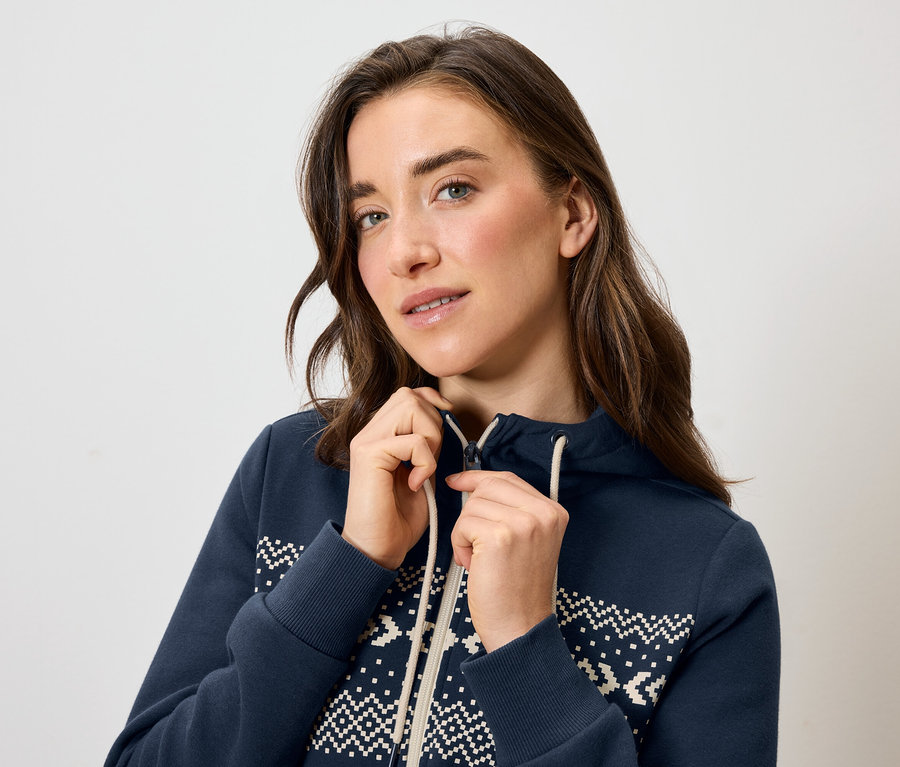 Eine Frau schließt eine blaue Kapuzenjacke mit einem weißen Muster.
