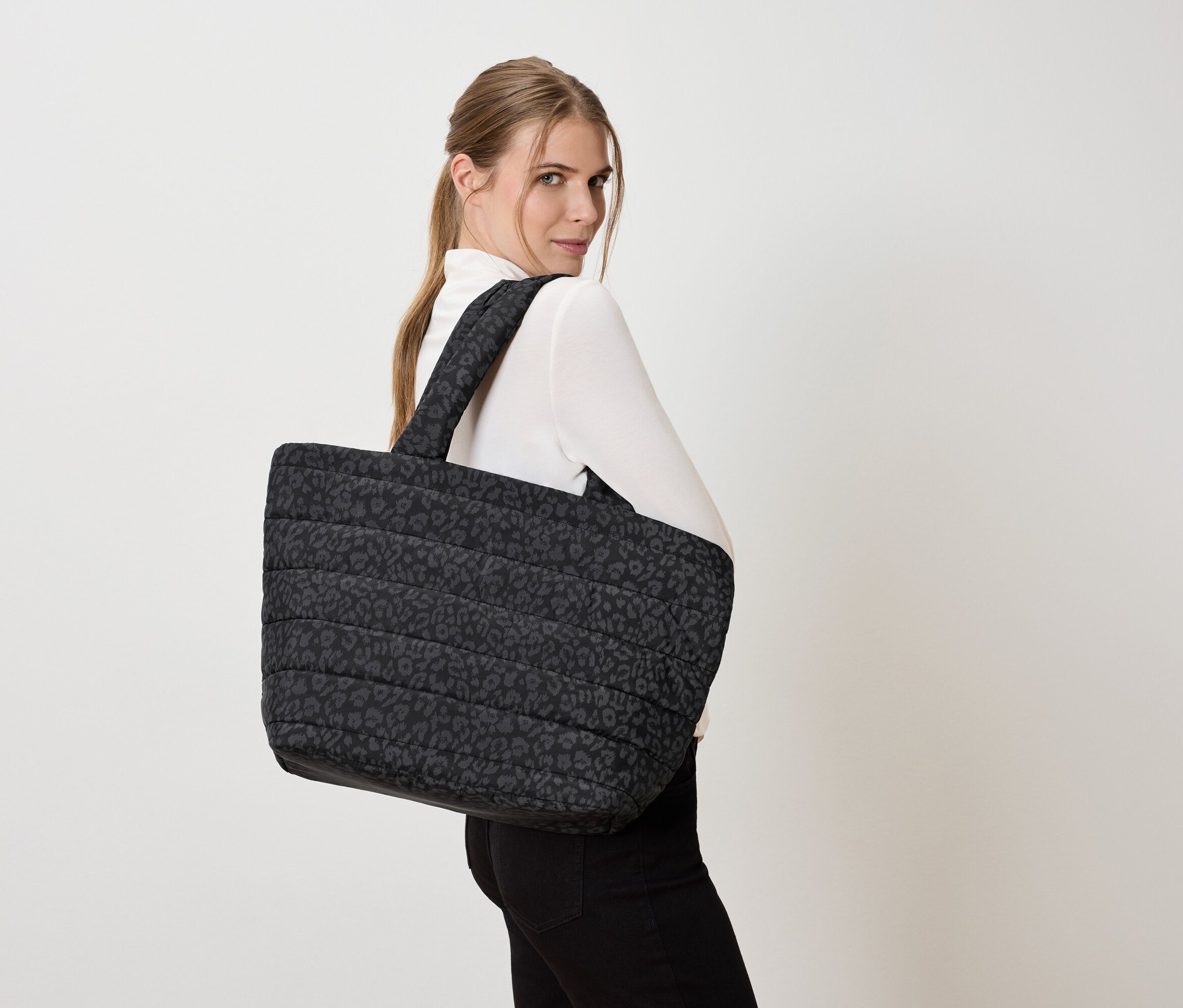 Frau mit einer großen, gesteppten Tragetasche mit Leopardenmuster über der Schulter.