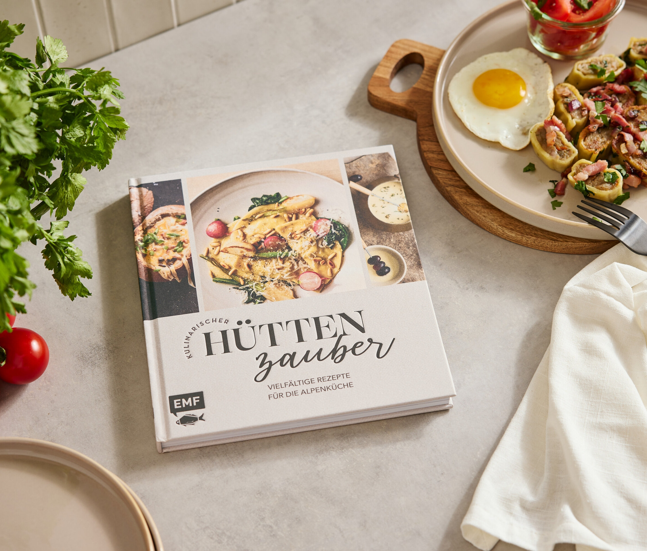 Auf einem Tisch liegen ein Kochbuch, ein Teller mit Essen, ein Ei, ein Glas mit Tomaten, Petersilie und Tomaten.