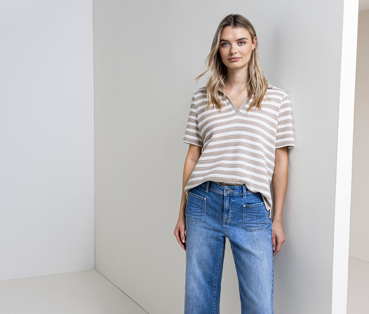 Frau posiert in Jeans und gestreiftem Street One Strickshirt vor einer Wand.