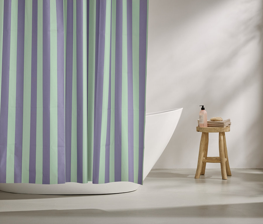Gestreifter Duschvorhang in Lila und Mintgrün hängt vor einer Badewanne. Auf einem Hocker stehen Badutensilien.