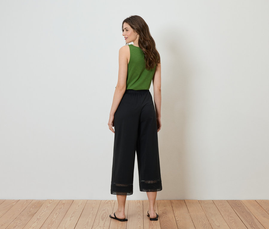 Eine Frau steht mit dem Rücken zur Kamera, sie trägt ein grünes Top und eine schwarze Culotte mit Spitze am Saum.