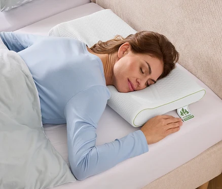 Frau schläft auf einem strukturierten, weißen Kissen mit grünen Akzenten in einem Bett mit hellblauem Bezug.