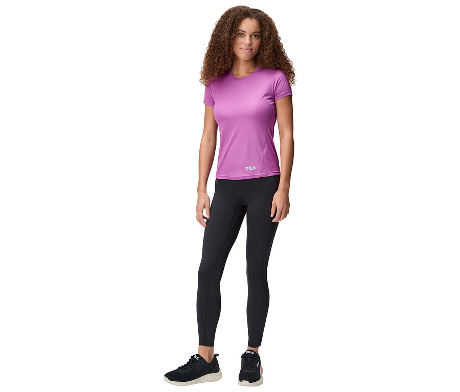 Frau steht, trägt ein violettes Fila-T-Shirt, schwarze Leggings und schwarze Turnschuhe.