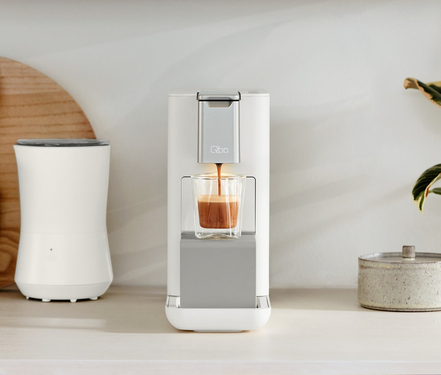 Auf einer Küchentheke stehen Qbo ESSENTIAL Bright Sand und Qbo ICONIC Dark Chrome Kaffeemaschinen.
