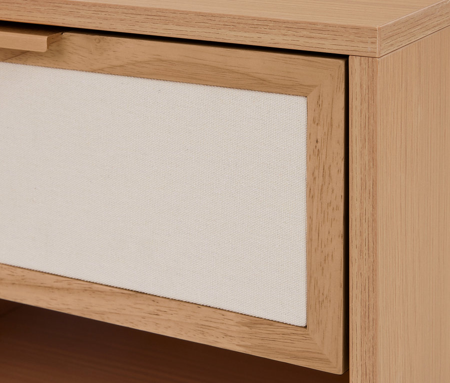 Nahaufnahme einer hellen Holzschublade mit cremefarbener Stofffront und einem kleinen Holzgriff.
