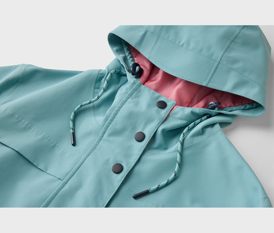 Nahaufnahme einer türkisfarbenen Jacke mit pinkem Futter. Die Jacke hat eine Kapuze mit Kordelzug, eine Knopfleiste mit drei schwarzen Knöpfen und einen türkis-schwarz gestreiften Kordelzug am Kragen.