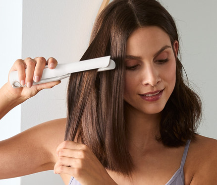Frau glättet ihr Haar mit einem kabellosen Haarglätter.