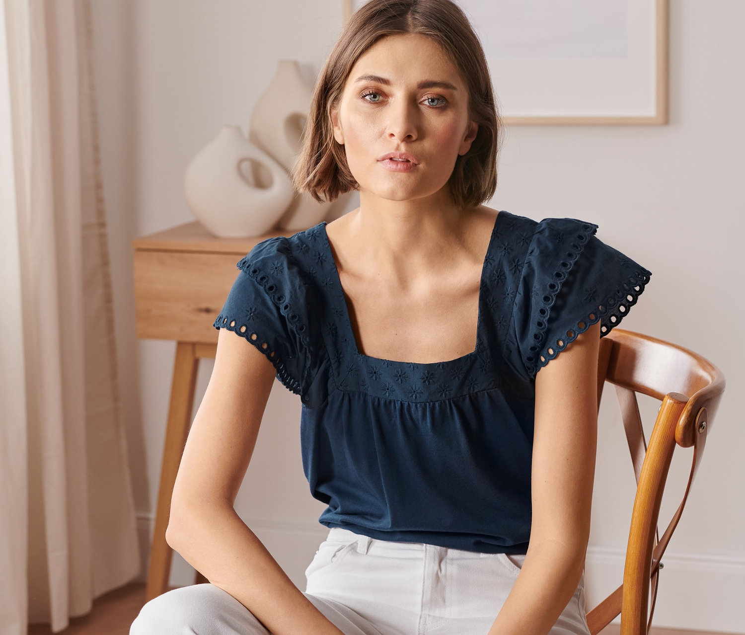 Frau sitzt auf einem Stuhl und trägt ein dunkelblaues Shirt mit Stickerei.