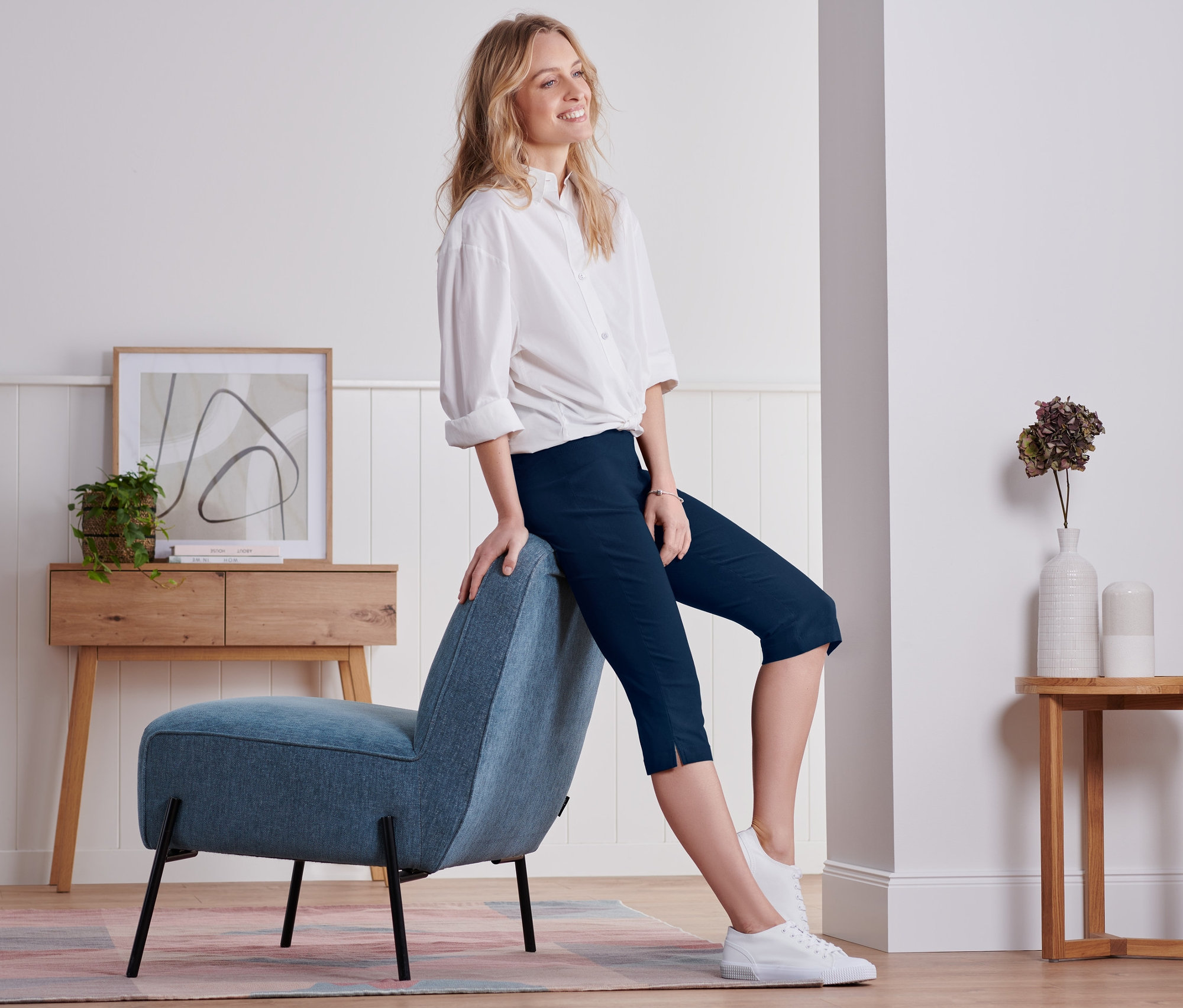 Frau sitzt seitlich auf blauem Sessel, trägt eine marineblaue 3/4-Bengalin-Hose.