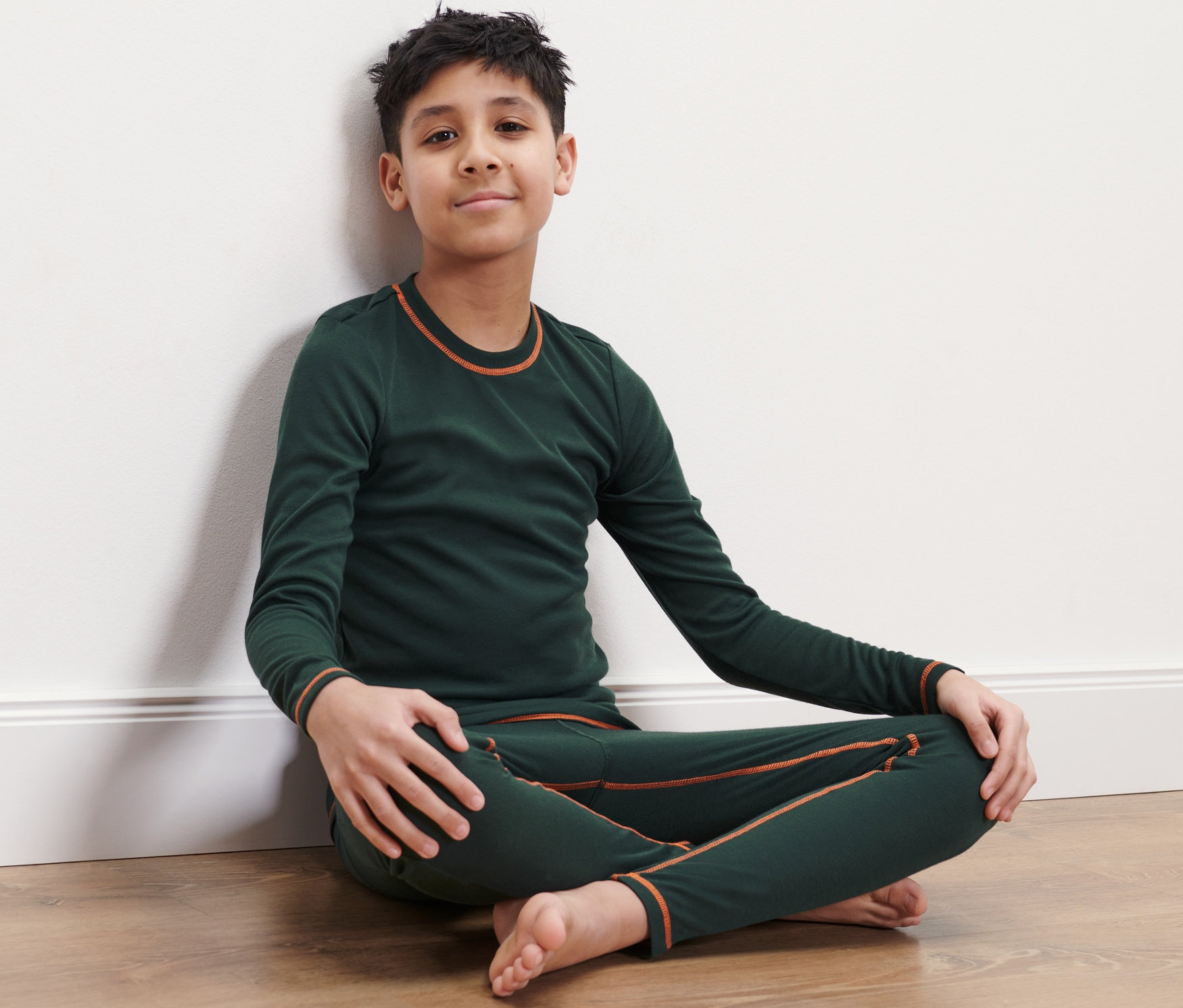 Ein Junge sitzt in Kinder-Ski-und-Winter-Unterwäsche auf dem Boden.