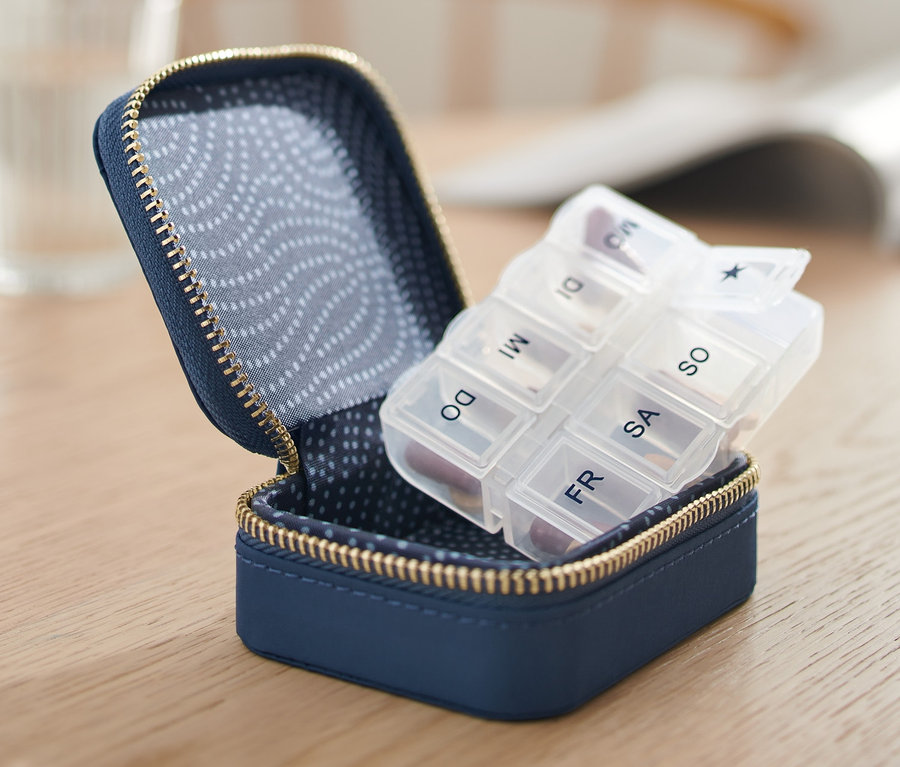 Geöffnete blaue Pillendose mit Hülle auf einem Holztisch.