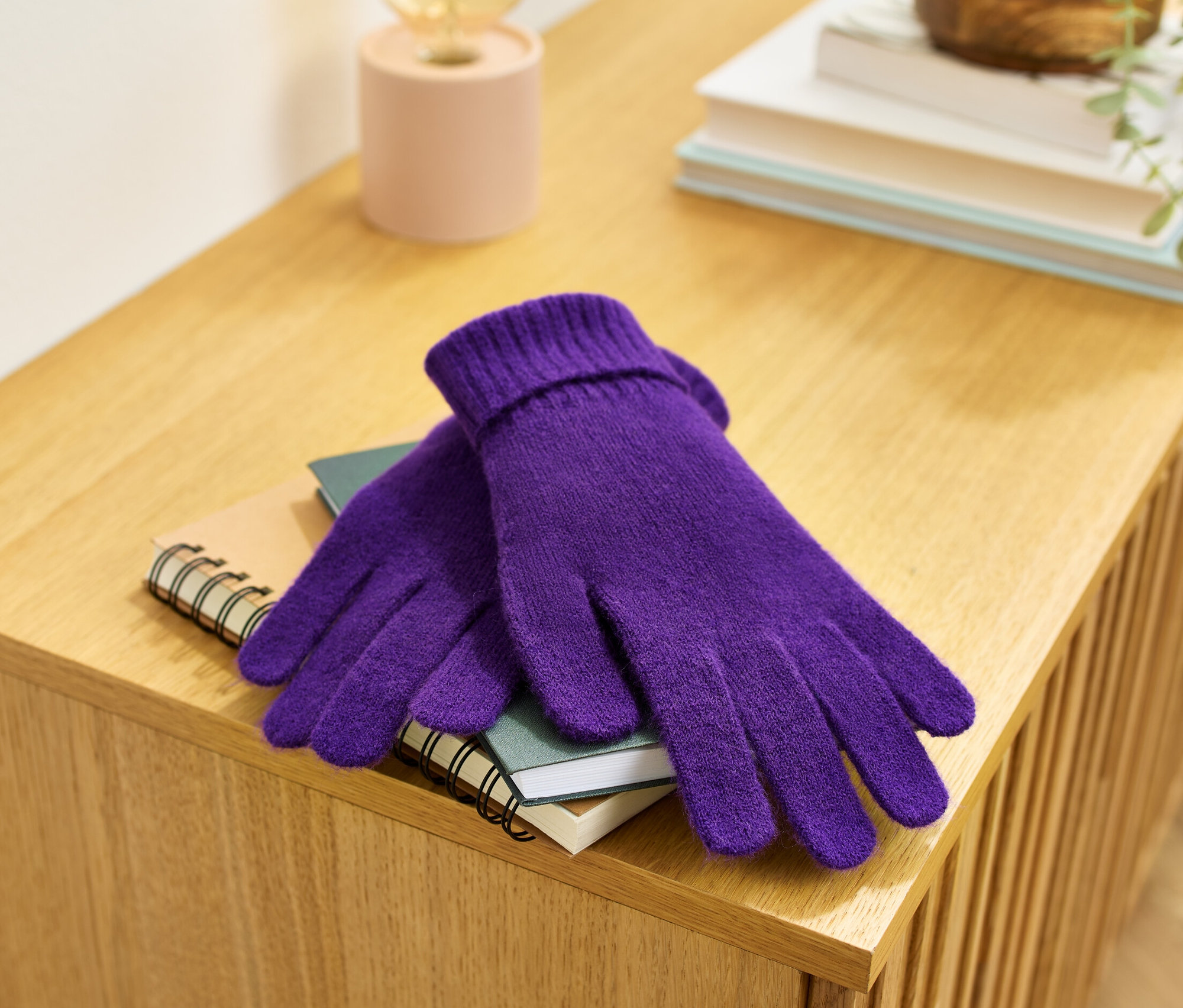 Lila Strickhandschuhe liegen auf einem Notizbuch auf einer Holzkommode.