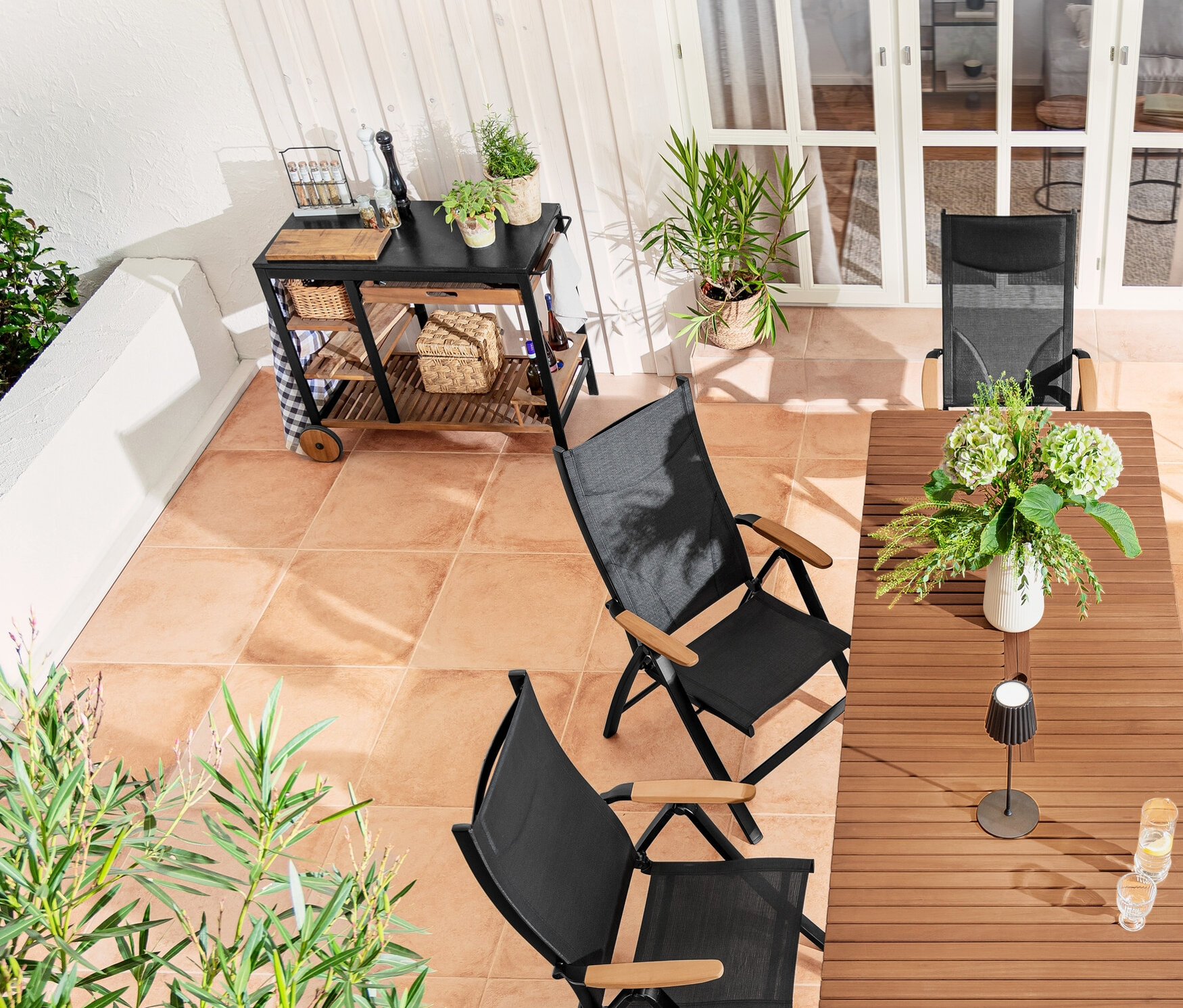 Außenterrasse mit Ausziehtisch »Elin«, 2-in-1-Dining-Bank-Liege »Elin«, Hochlehner, schwarzer LED-Akku-Outdoor-Stehleuchte und Pflanzkasten-Raumteiler »Tinus«.