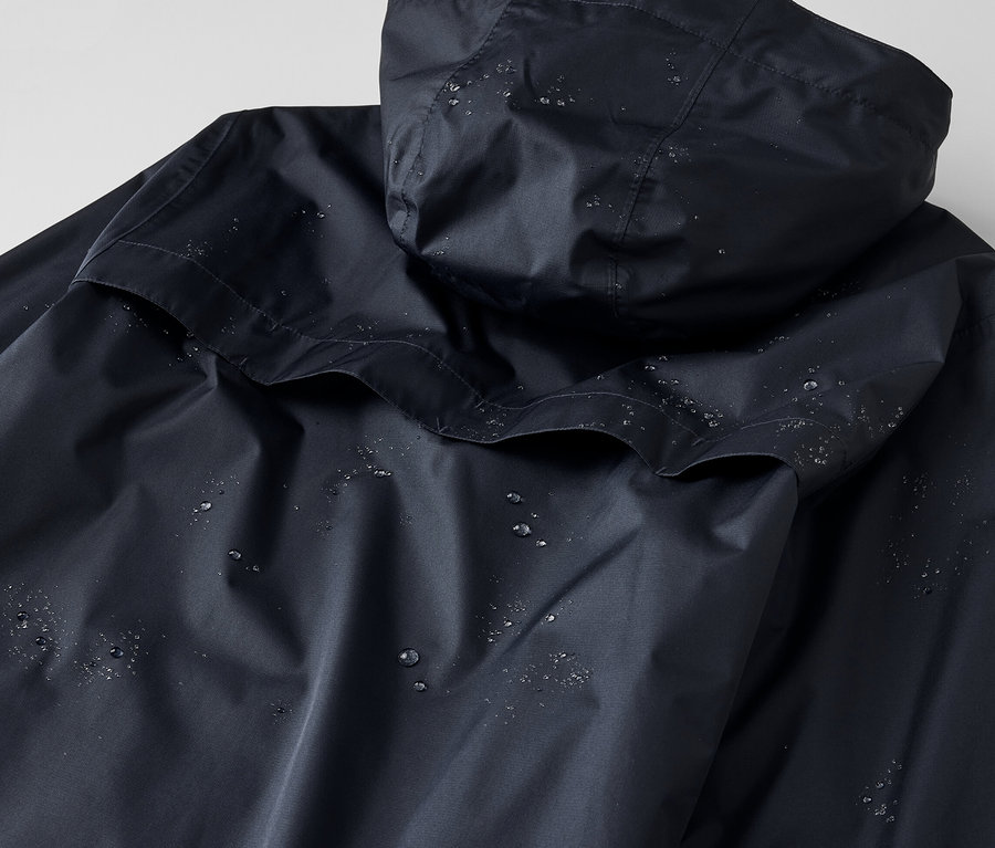 Detailansicht einer Unisex-Regenjacke mit Kapuze, auf der sich Wassertropfen befinden.