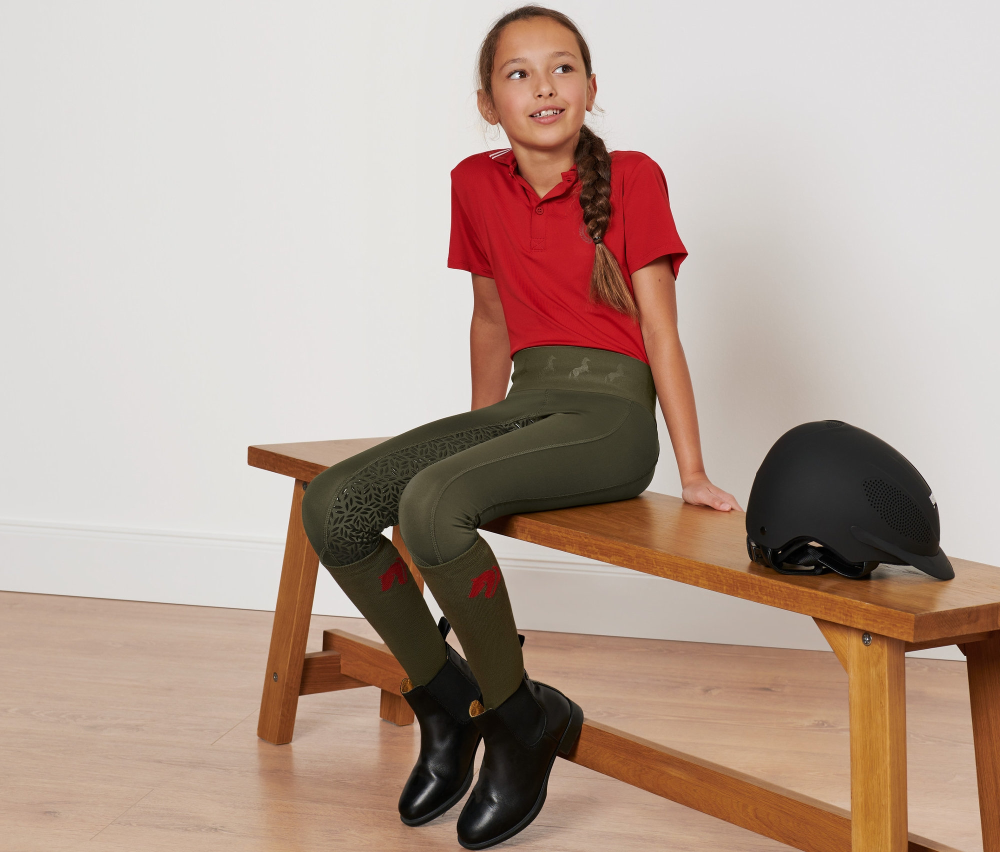 Ein Mädchen sitzt auf einer Bank und trägt eine grüne Kinder-Grip-Vollbesatz-Reittight.
