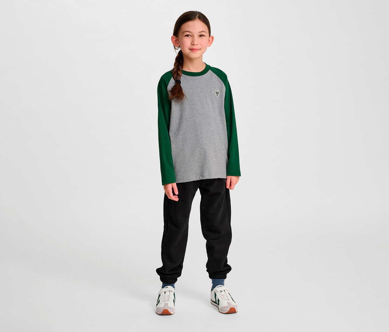 Mädchen steht und trägt ein grünes HUMMEL HMLJR Raglan Loose T-Shirt BEE.