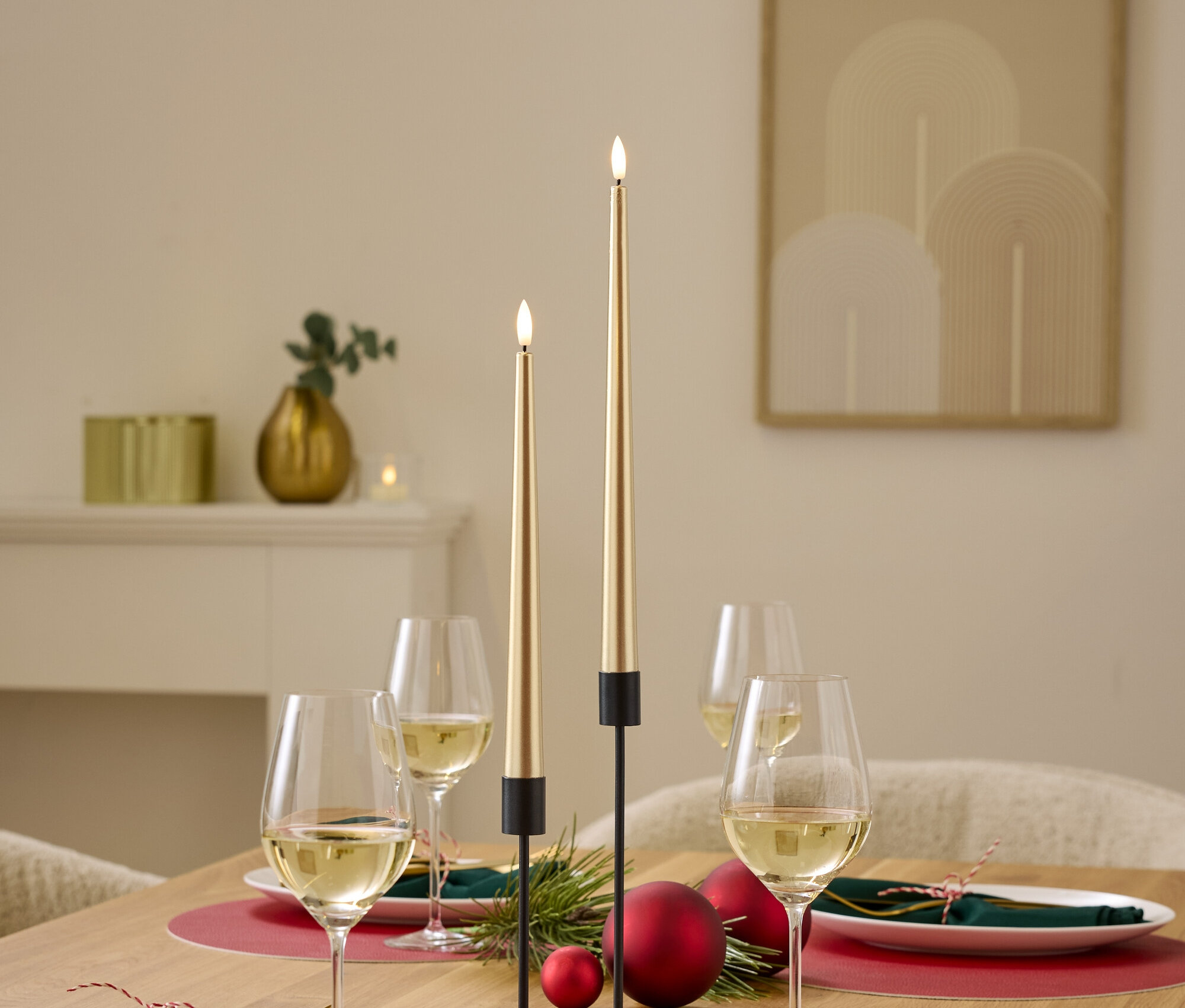 Festlich gedeckter Tisch mit Tellern, Weingläsern, Servietten, roten Ornamenten und goldenen Kerzen.