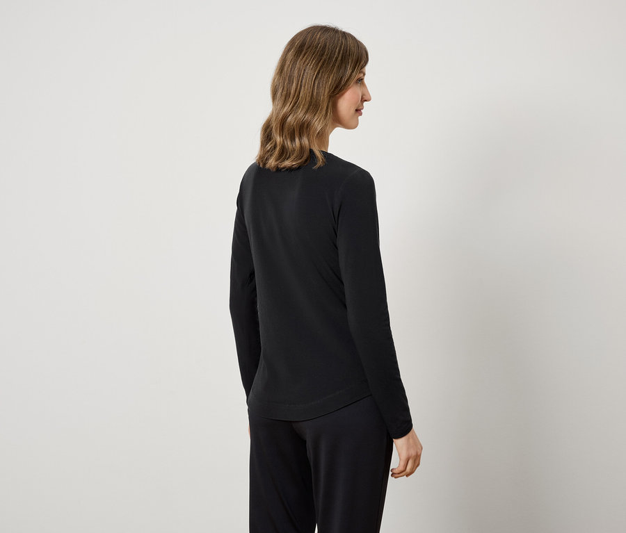 Eine Frau von hinten trägt ein schwarzes Langarmshirt und eine schwarze Hose.