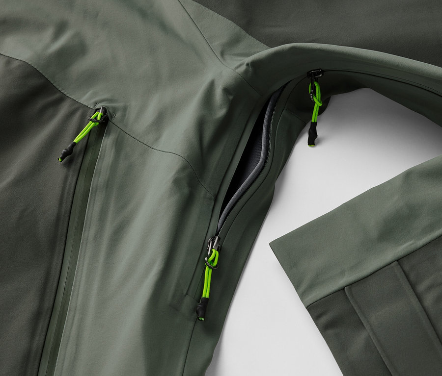 Detailaufnahme einer 3-Lagen-Outdoorjacke mit geöffneter Tasche und neon-grünen Reißverschlussdetails.