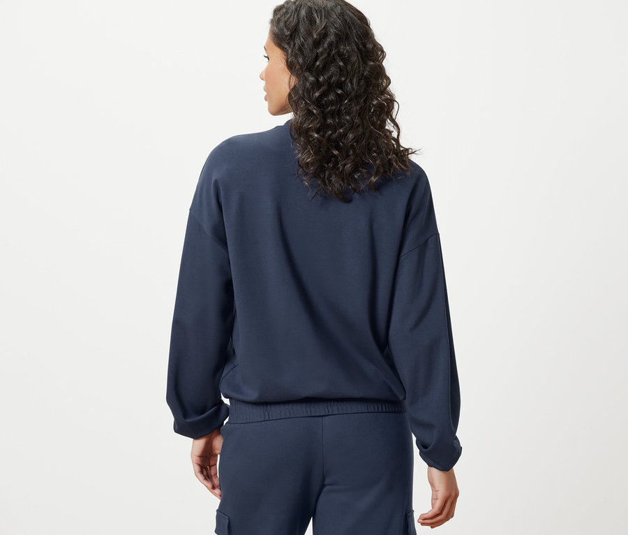 Rückansicht einer Frau mit dunklem, gewelltem Haar, die eine marineblaue Sweatjacke trägt.