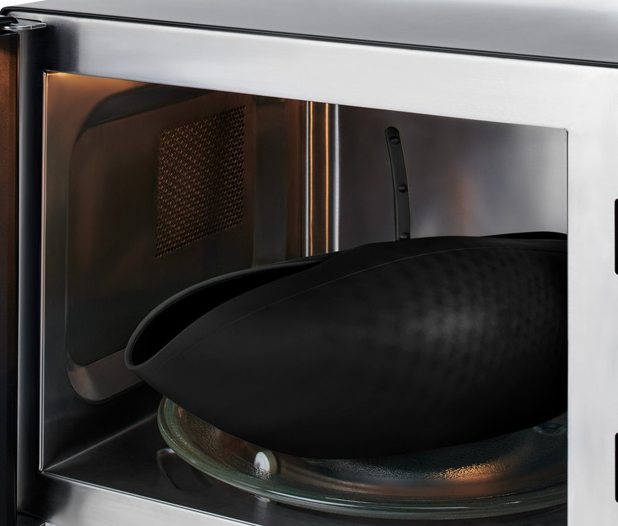 Eine schwarze Silikonform liegt auf einem Glasteller im Inneren einer geöffneten Mikrowelle.