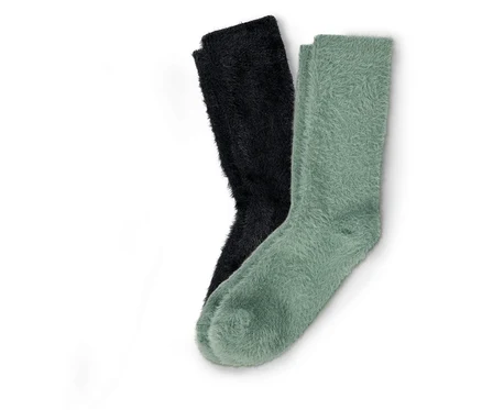 Zwei Paar flauschige Socken, ein Paar schwarz und ein Paar hellgrün, liegen nebeneinander auf einem weißen Hintergrund.