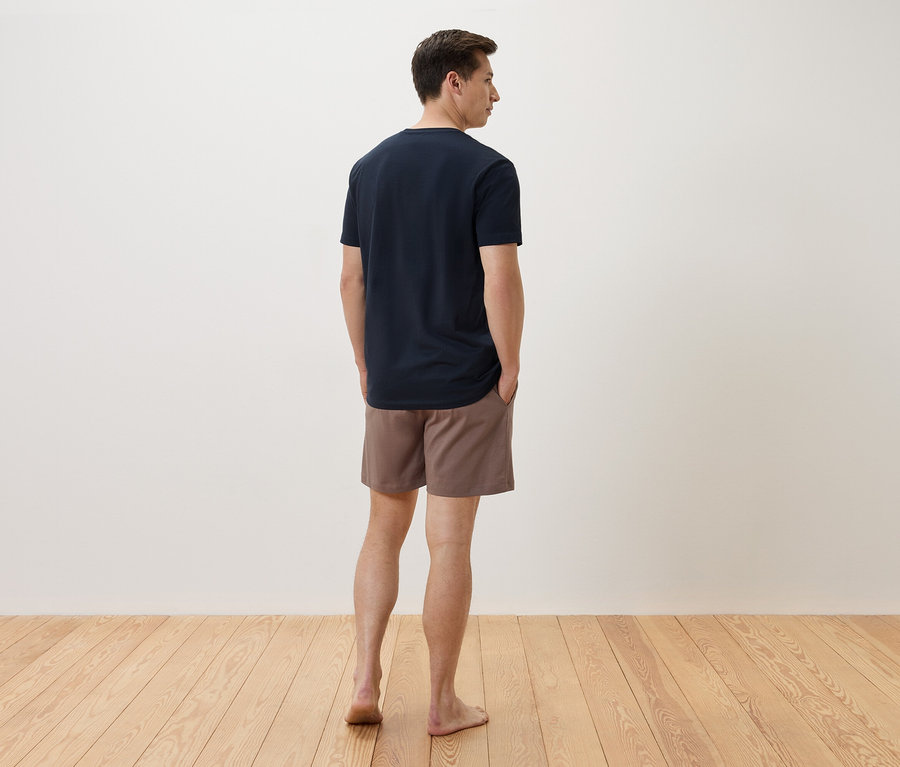 Ein Mann steht mit dem Rücken zur Kamera, er trägt ein marineblaues T-Shirt und braune Shorts.