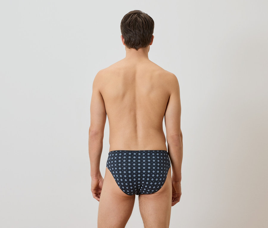 Ein Mann von hinten, der eine dunkelblaue Badehose mit einem weißen Blumenmuster trägt.