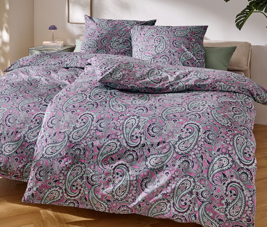 Nahaufnahme eines Bettes mit rosa Paisley-Muster-Bettwäsche.