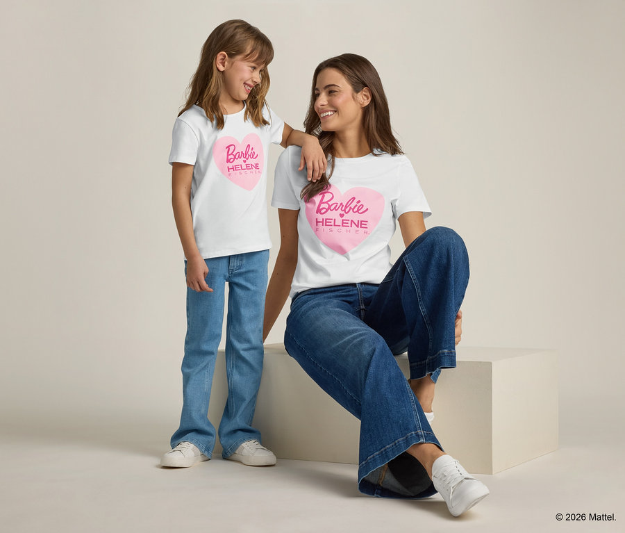 Mädchen lehnt an der Schulter einer Frau, beide tragen weiße T-Shirts mit rosafarbenem Barbie-Herz und Jeans.