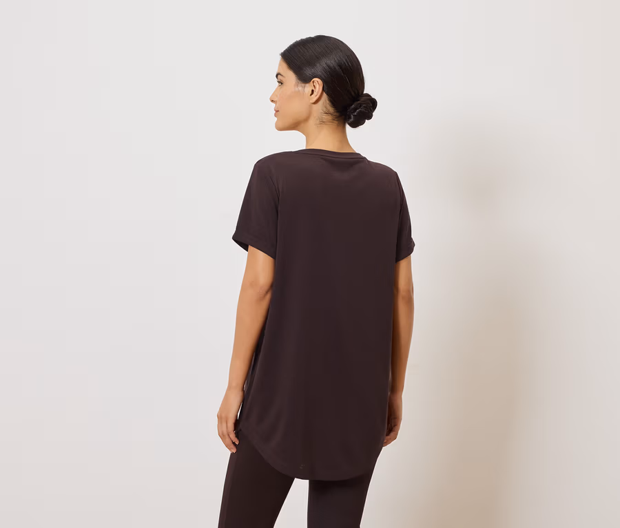 Frau von hinten in braunem T-Shirt und Leggings vor weißem Hintergrund.