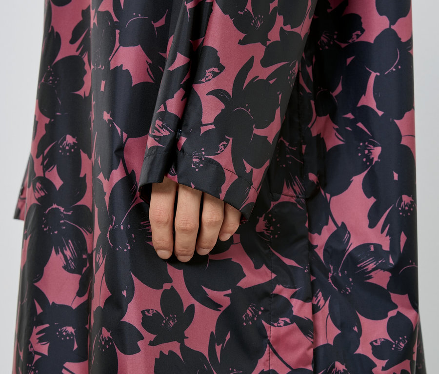 Nahaufnahme eines Arms und eines Teils eines Mantels mit Blumenmuster in Schwarz auf Rosa.