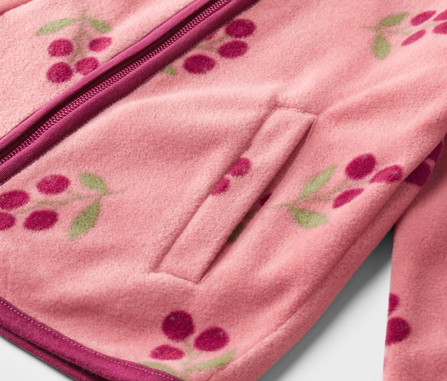 Nahaufnahme einer rosa Fleecejacke mit Reißverschluss, Tascheneingriff und Kirschmuster.