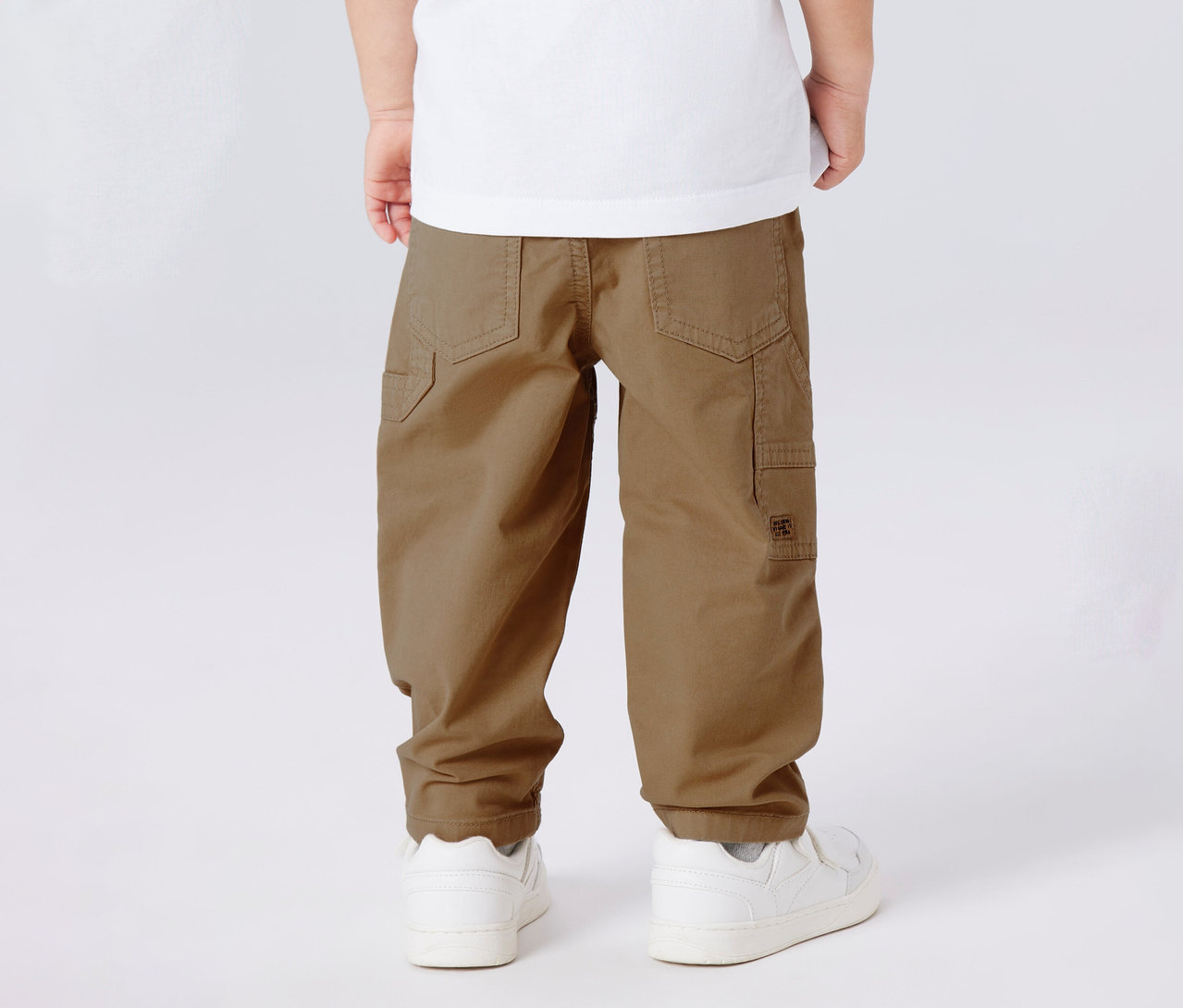 Nahaufnahme der Rückseite eines Kindes, das eine NAME IT Kinder-Twillhose und weiße Turnschuhe trägt.