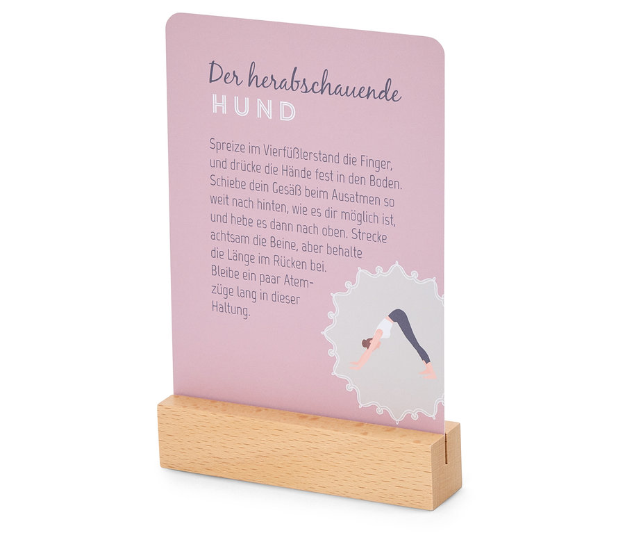 Eine Karte mit der Beschreibung der Yoga-Position "Herabschauender Hund" steckt in einem Holzfuß.
