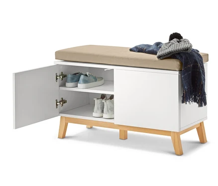 Geöffnete, weiße Sitzbank mit Stauraumfächern, auf der Schuhe, eine Decke und eine Mütze liegen.