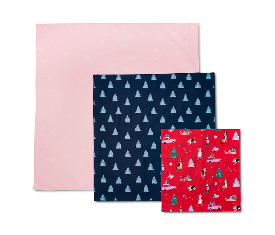 Rosa Stoff-Geschenkpapier mit weißen Sternen, dunkelblaues mit weißen Bäumen und rotes mit Weihnachtsmotiven.