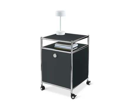 Ein schwarzer Rollcontainer Metall »CN3« mit Klappe, mit Lampe und Büchern darauf.