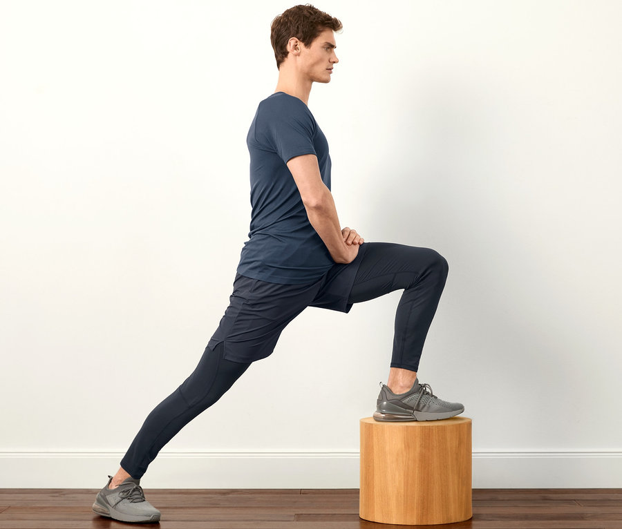 Mann in marineblauem T-Shirt und Tight dehnt sich auf einem Holzhocker.