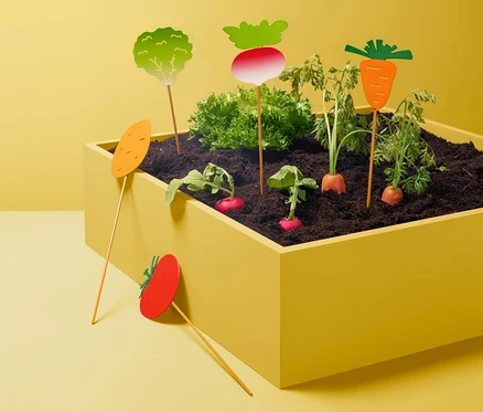 Gemüse wächst in einem gelben Blumentopf, Beetstecker »Gemüse« stecken in dem Beet.
