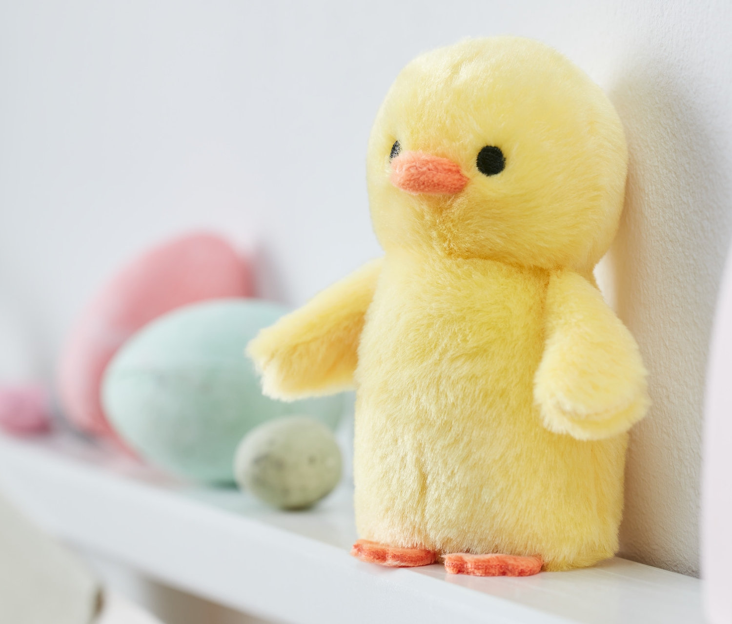 Gelbes Küken mit Sound steht auf einem weißen Regal neben dekorativen Ostereiern und einem hölzernen Regenbogenspielzeug.