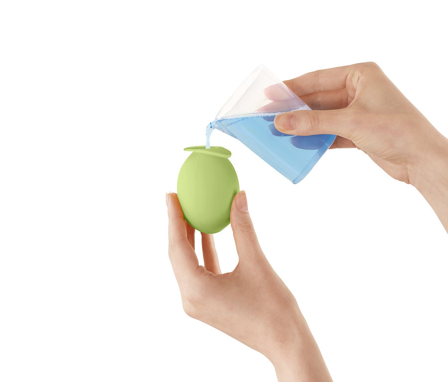 Frau giesst Flüssigkeit aus einem Messbecher in einen hellgrünen Entkalker-Aufsatz für Wasserhähne.