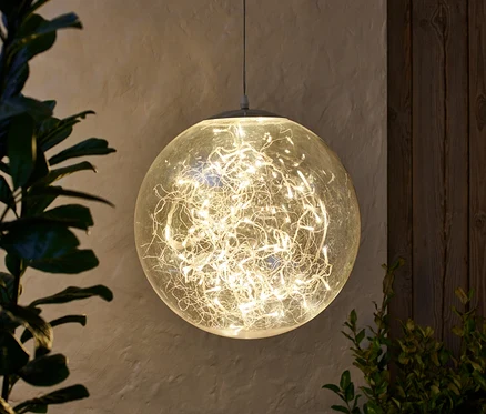 Eine hängende LED-Kugel, ca. 40 cm, beleuchtet, neben Pflanzen.