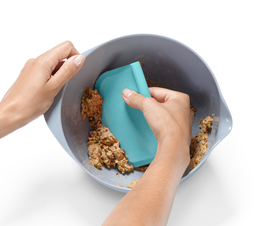 Händisches Mischen von Teig in einer Schüssel mit einem blauen Spatel aus einem Backhelfer-Set.