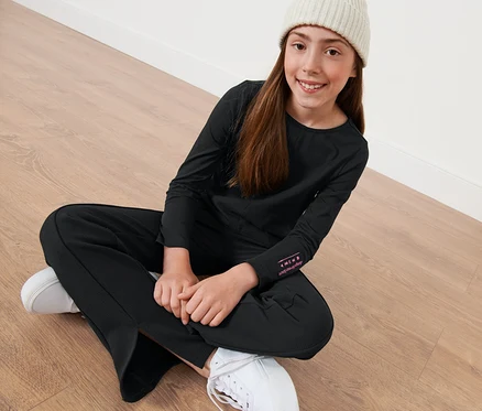Mädchen sitzt auf dem Boden und trägt ein schwarzes Kinder-Langarmshirt.